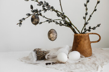 Easter rustic still life. Natural eggs, feathers, nest, willow branches in vase on aged wooden table. Simple stylish easter decoration on table aesthetics. Happy Easter
