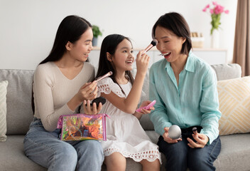 Makeup spa day concept. Adorable little girl Asian with mother and granny applying cosmetics on sofa at home