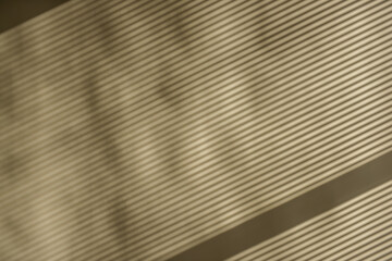 Obraz premium On the khaki wall, the lines from the window blinds are a light shadow. Texture background, pattern