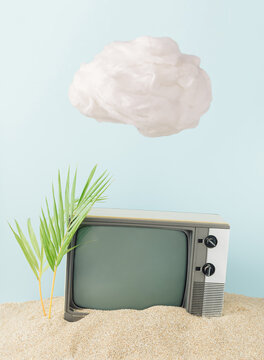 Retro scene made with old television and fresh palm leaves on sand and white cloud. Creative vintage technology concept.
