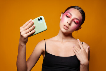 Young beautiful woman looks at the phone bright makeup posing fashion emotions yellow background unaltered