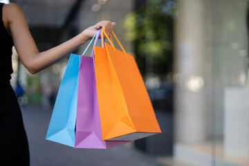Close-up of multicolored blue, purple, and orange shopping bags in an African-American woman's hand outdoors in front of a mall