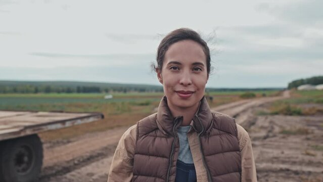 Medium close-up portrait of beautiful young adult woman working in modern farm standing outdoors looking at camera. Suitable for deepfake generation or face swap