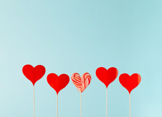 Fototapeta na wymiar Red paper hearts on the wooden sticks with a heart-shaped lollipop in between on a blue background. 