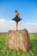 Girl in a flying dress on a bale of hay