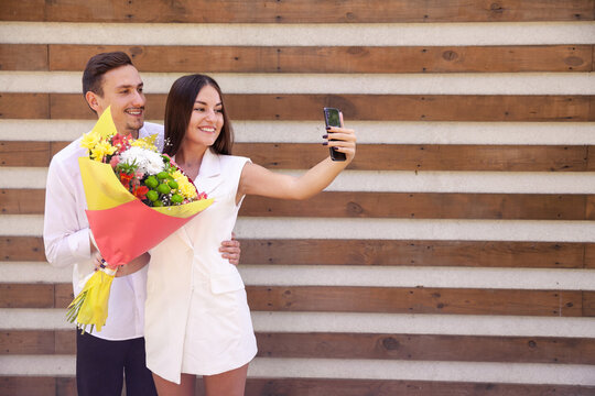 marriage, technology, lifestyle and people concept - Wedding of a European couple in love with a large bouquet talking on a video call with relatives on a brown ribbed background with copy space