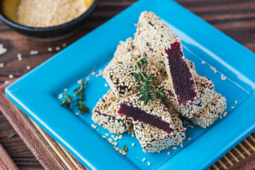 Sweetness, square beet marmalade in sesame sprinkling on a blue plate on a brown wooden background. Korean cuisine.