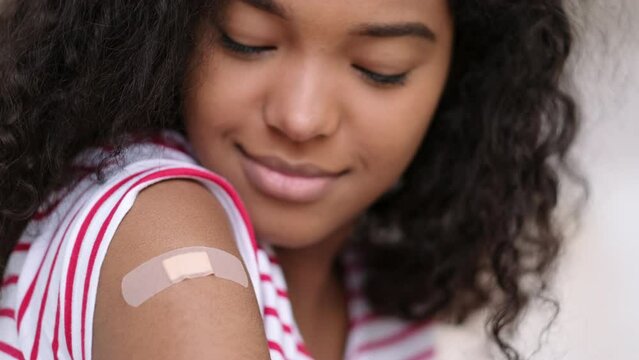vaccinated African American woman showing arm with medical plaster patch Plaster On Shoulder, black female after getting vaccine dose against covid. Healthcare immunization, coronavirus vaccination