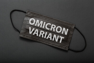 Omicron positive text warning sign on medical protective black mask. New Omicron variant covid 19 on face mask isolated on black background.