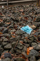 A lonely blue face mask thrown away on some stones.