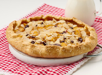baked round pie with apple pieces, sprinkled with almond flakes on a white table