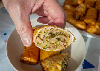 The cook holding a half cut home made crispy spring roll showing the meat and vegetable filling inside.