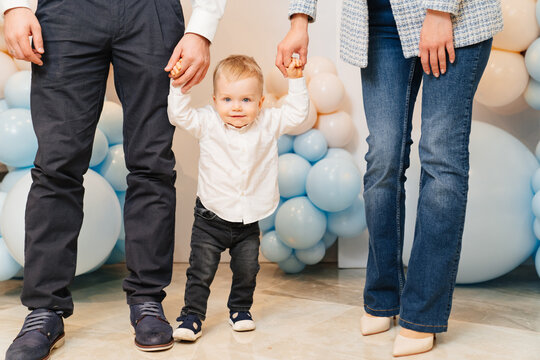 boy holds father and mother by hands in front of photo zone with balloons