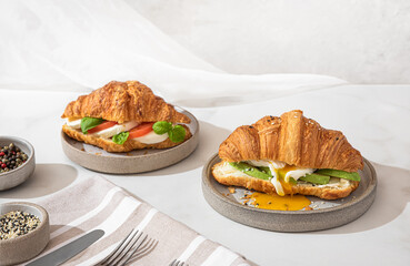 Tasty breakfast with croissant sandwiches with poached egg, avocado, soft cheese, mozzarella and tomato