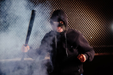 Masked angry man with bat in smoke