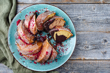 Traditional exotically bundt marble cocoa chocolate cake with icing sugar glaze and freeze dry raspberry topping served as top view on a Nordic design plate with copy space