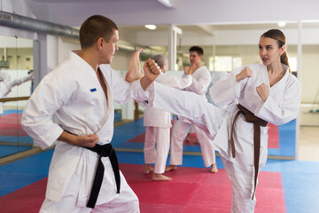 Woman and man in white kimono and belts sparring during karate training.