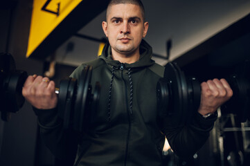 Fototapeta na wymiar Man training in the gym and lifting dumbbells