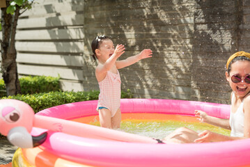 A toddler splashes water on her mother as both play in an inflatable pink pool in a sunny day in the garden of a house in Edinburgh, Scotland, United Kingdom