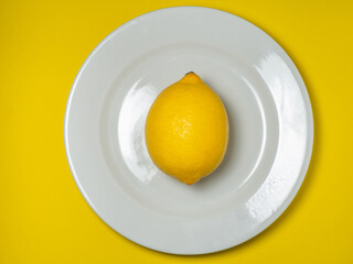 A whole lemon on a plate on a yellow background. Citrus on the table. Bright background. Healthy fortified food for a diet.