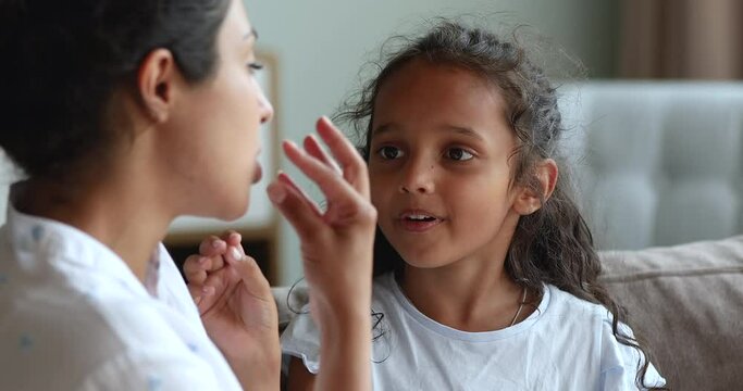 Close up stuttering 6s Indian girl do exercises with speech therapist, train articulation, pronounces repeat words correctly, engaged in voice pronunciation class together at home. Development concept