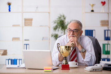 Old male employee being awarded with golden cup