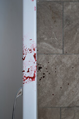 Close up shot of side of a bath. Blood smeared on the edge near the handle and blood drops on the floor tiles. Bathroom setting with copy space. Crime and violence concept image.