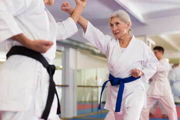 Senior woman in kimono exercising with sparring-partner during group karate training. © JackF