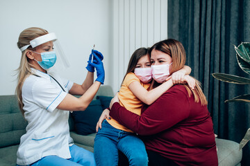 A mother hugs her frightened daughter while a nurse vaccinates her.