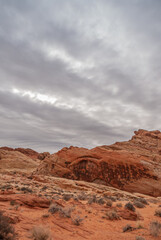 Overton, Nevada, USA - February 25, 2010: Valley of Fire. Portrait, Heavy rainy gray cloudscape gathers over red rock mountainous area cropping out of dry red desert floor with greenish shrubs.