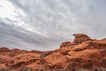 Fototapeta na wymiar Overton, Nevada, USA - February 25, 2010: Valley of Fire. Landscape with bird chick like rock on top of plateau of blackend red rocks under heavy gray cloudscape.