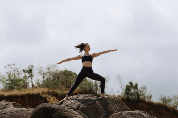 Woman doing yoga exercise asana pose on a top of a mountain cloud sky.
