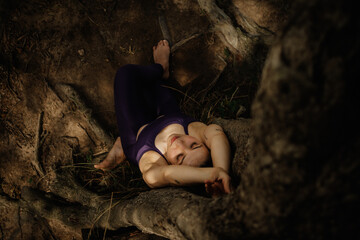 Woman doing yoga exercise pose under a tree at the earthly ground sitting on the roots