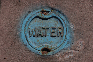 Close-up view of a blue painted water valve cover in the street pavement