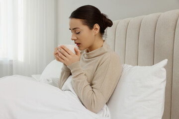 Sick young woman with cup of hot drink in bed at home