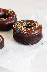 Rich chocolate baked doughnuts with colorful sprinkles on a naking paper.