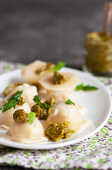 Homemade ravioli stuffed with chicken meat  and pesto sauce in a white plate on a grey background.
