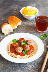 Spaghetti with meatballs and tomato sauce in a white plate on a gray background. Close up.