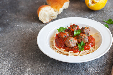Spaghetti with meatballs and tomato sauce in a white plate on a gray background. Close up.