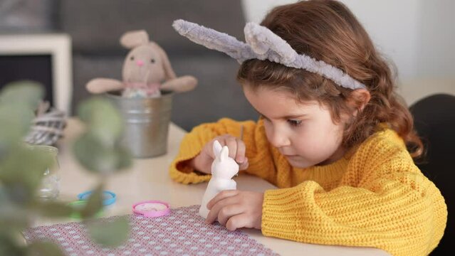 Cute little girl in bunny ears making decorations for Easter at home. Traditional Easter party preparation and decoration concept