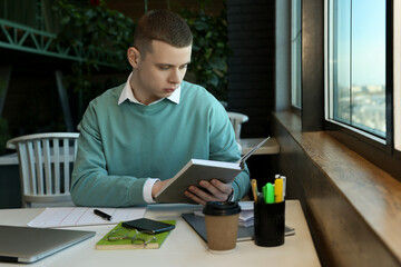 Young male student with books studying at table in cafe