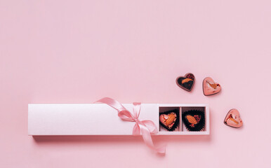 Chocolate candy hearts festive box satin ribbon bow on pink background. Flat layout copy space. Holiday concept