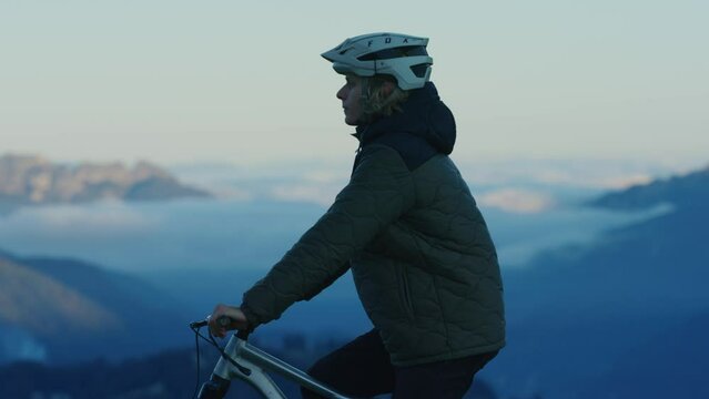 A mountain biker is resting above a sea of clouds at sunset