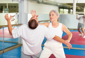 Fototapeta na wymiar Senior European woman learning chin strike move on man during self-defense training.