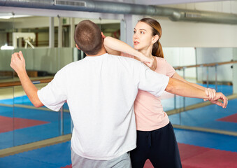 Caucasian woman performing elbow strike while sparring with man in gym during self-defence training.