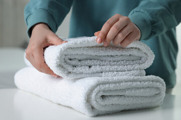 Woman touching soft white towel indoors, closeup