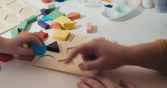 Child with his mother collects wooden constructor - puzzle, close up shot, a rear view, no faces are visible. The concept of development, joint family pastime and education of the child in playful way