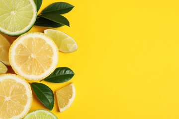 Fresh ripe lemons, limes and green leaves on yellow background, flat lay. Space for text