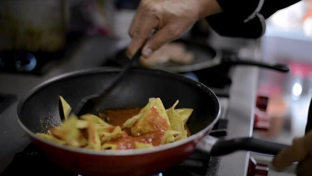 Chef sou-chef preparing a traditional mexican dish called chilaquiles mixing fried tortilla chips with hot tomato sauce in a pan at a local cafe diner restaurant in latin america