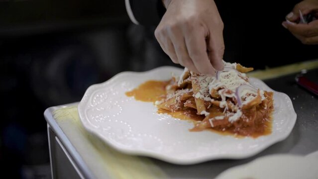 Chef sou-chef cook preparing a traditional mexican dish called chilaquiles adding sliced onion on top at a local cafe diner restaurant in latin america